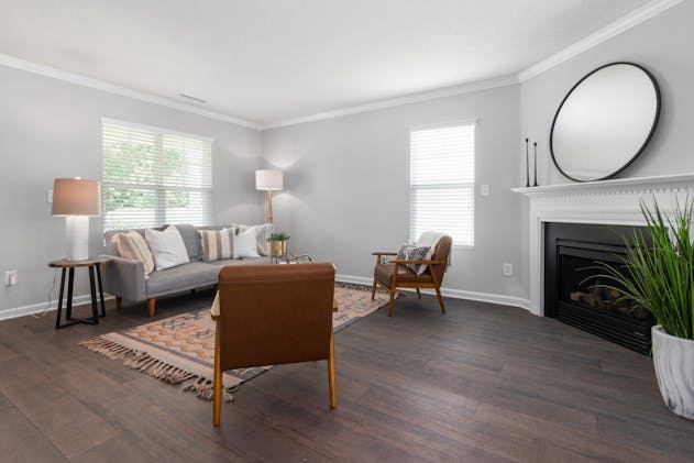 a grey living room with dark wood flooring a couch and two arm chairs